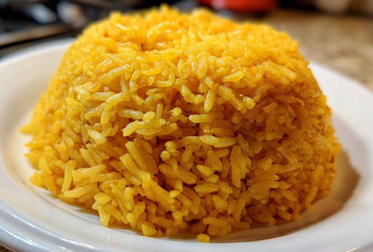 A mound of bright yellow, fluffy turmeric rice served on a white plate, ready to eat.
