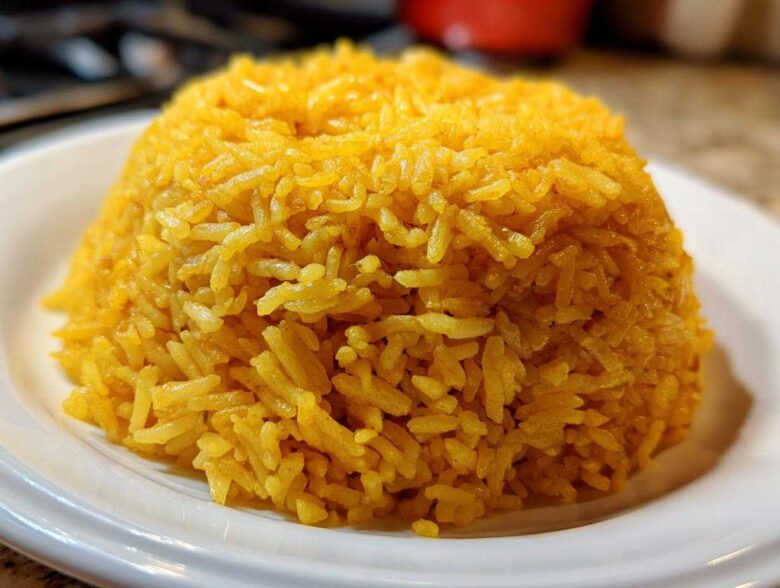 A mound of bright yellow, fluffy turmeric rice served on a white plate, ready to eat.