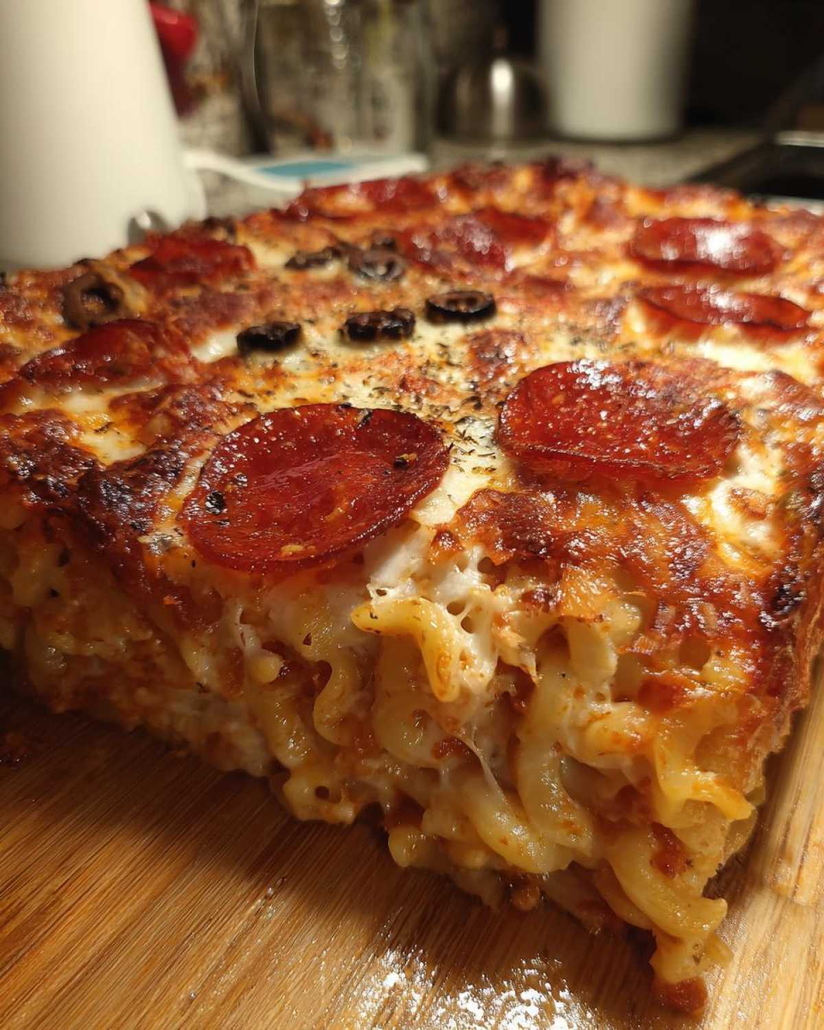Close-up of a thick slice of baked pizza pasta casserole with melted cheese, pepperoni, and olives.