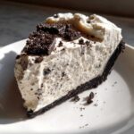 A decadent slice of no-bake Oreo pie with a dark crust and creamy white filling, topped with cookie pieces.