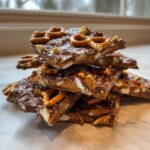 A stack of broken pieces of peanut butter pretzel bark topped with pretzels, nuts, and sea salt.