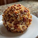 A delicious, round cheese ball recipe coated entirely in chopped pecans served on a white plate.