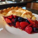 A close-up of a perfect slice of berry pie showing strawberries, blueberries, and raspberries in a juicy filling.