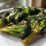 Close-up of perfectly crisp roasted broccoli florets seasoned with cheese and spices on a white plate.