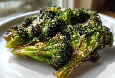 Close-up of perfectly crisp roasted broccoli florets seasoned with cheese and spices on a white plate.