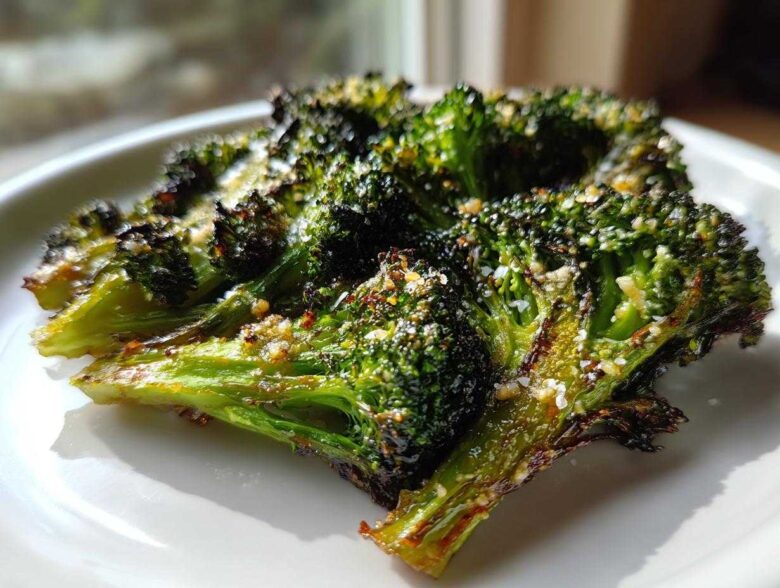 Close-up of perfectly crisp roasted broccoli florets seasoned with cheese and spices on a white plate.