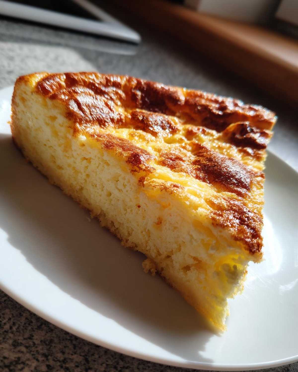 A thick, golden-brown slice of perfectly set egg custard resting on a white plate, illuminated by sunlight.