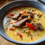 Close-up of a bowl of creamy philly cheese steak soup featuring strips of beef and colorful bell peppers.