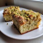 Close-up of two squares of moist pistachio coffee cake topped generously with chopped pistachios and streusel.