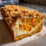 Close-up of a slice of pumpkin cream cheese bread showing the bright orange pumpkin cake, white cream cheese swirl, and crumb topping.