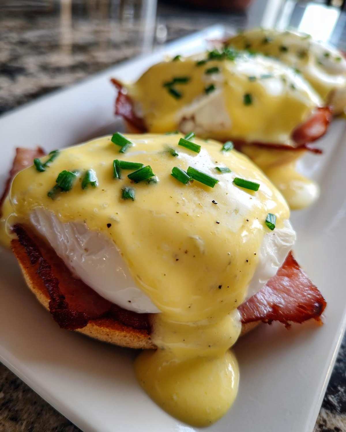 Close-up of perfectly poached eggs benedict smothered in hollandaise sauce and topped with fresh chives.