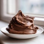 A generous swirl of rich, dark chocolate frosting piled high on a small white plate.