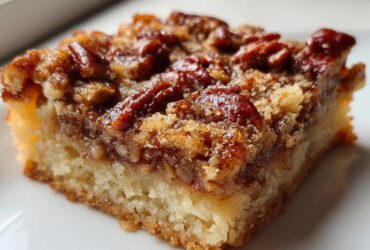A close-up, macro shot of a single serving of rich pecan pie bars showing the thick, buttery crust and gooey pecan topping.
