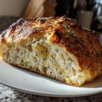 Cross-section of a rustic artisan bread loaf showing an open crumb structure and a dark, herbed crust.