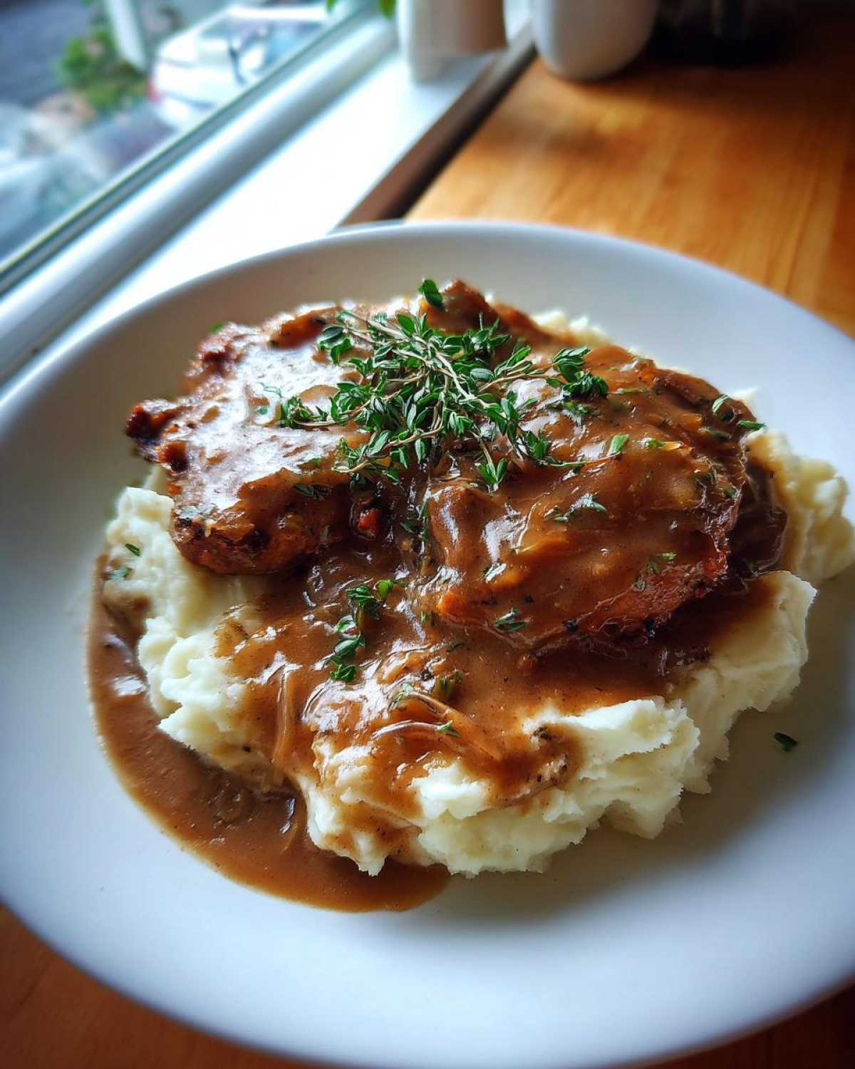 A close-up of savory chicken and gravy generously poured over a mound of fluffy mashed potatoes, garnished with fresh thyme.