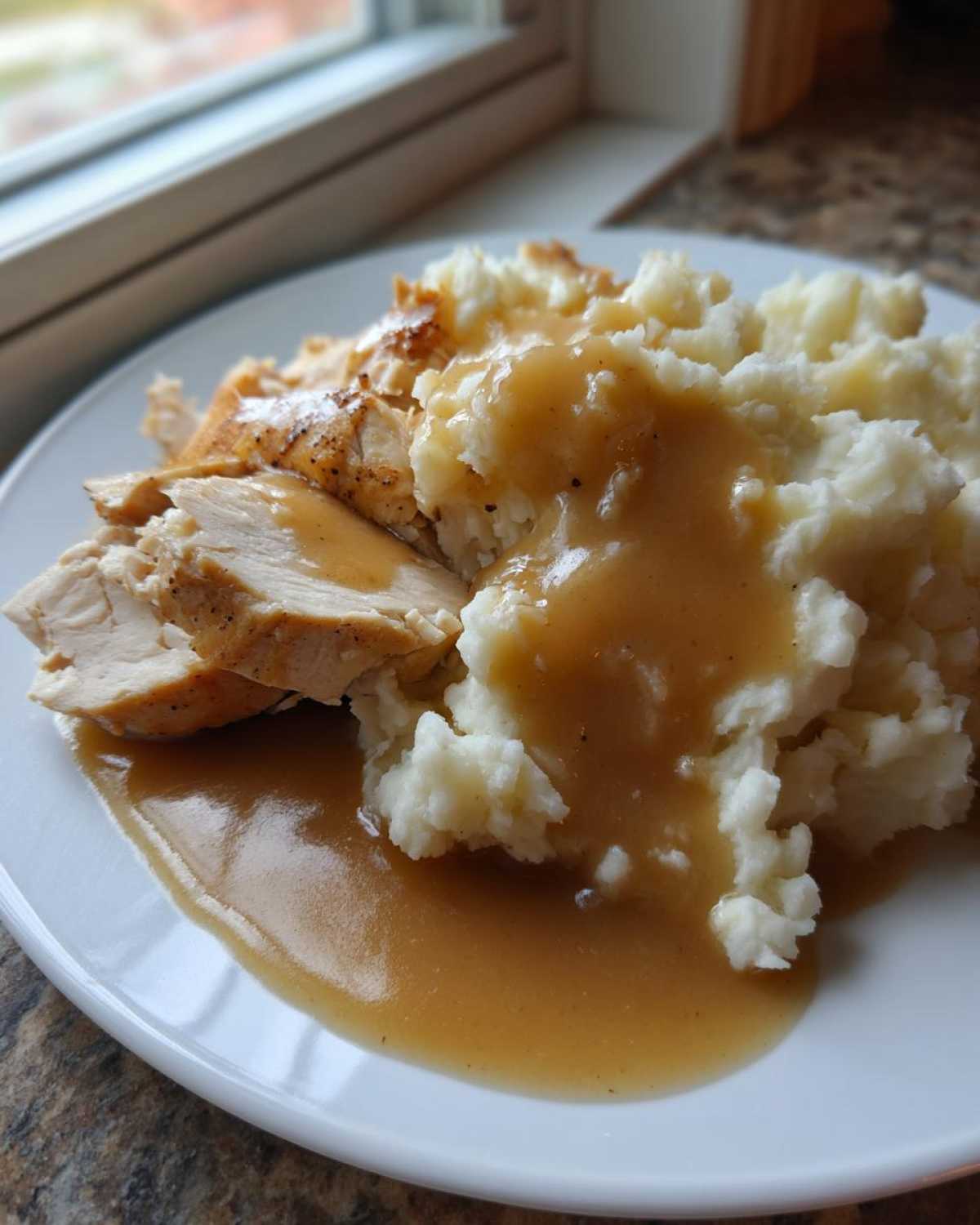 Close-up of sliced roasted chicken and fluffy mashed potatoes smothered in rich brown gravy, the perfect chicken and gravy dish.