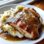 A close-up of perfectly cooked chicken and gravy served over a bed of creamy mashed potatoes.