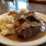 Close-up of tender meat covered in rich brown gravy served alongside creamy mashed potatoes, representing a savory chicken and gravy dish.