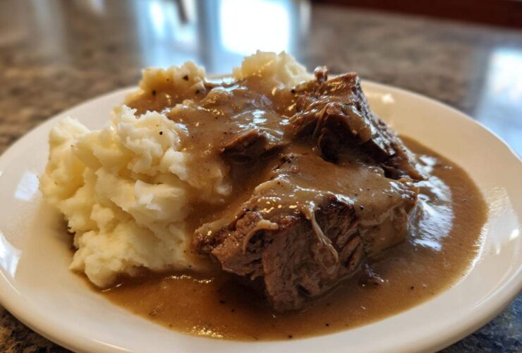 Close-up of tender meat covered in rich brown gravy served alongside creamy mashed potatoes, representing a savory chicken and gravy dish.