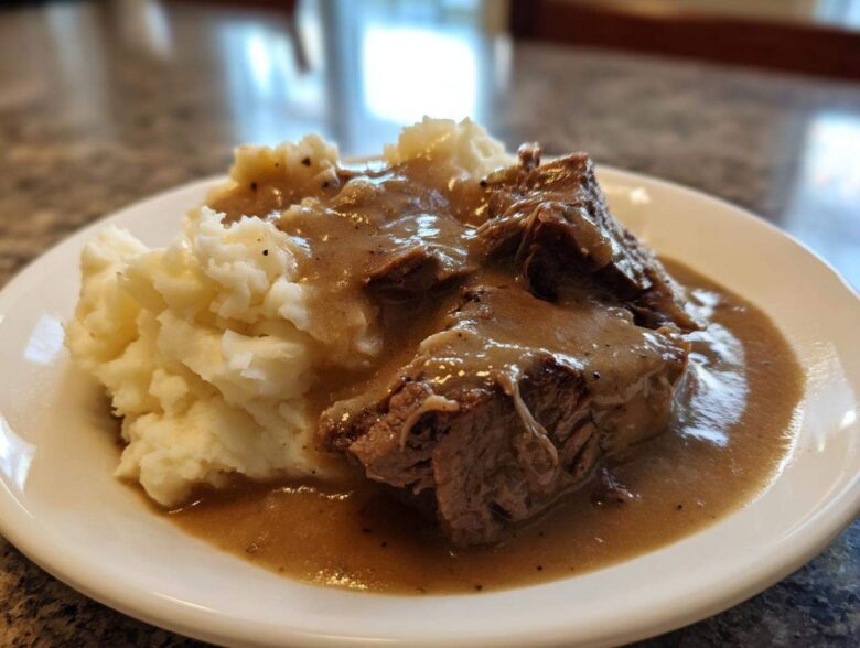 Close-up of tender meat covered in rich brown gravy served alongside creamy mashed potatoes, representing a savory chicken and gravy dish.