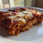 A close-up of a serving of easy chicken enchiladas covered in melted, bubbly cheese and red sauce on a white plate.