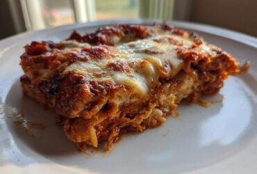 A close-up of a serving of easy chicken enchiladas covered in melted, bubbly cheese and red sauce on a white plate.