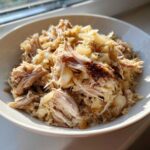Close-up of tender, shredded pork and sauerkraut mixture served in a white bowl, highlighting the texture.