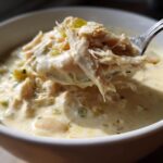 A spoonful of shredded white chicken being lifted from a bowl of creamy white chili.