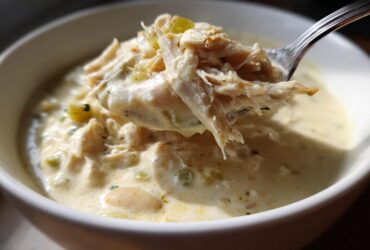 A spoonful of shredded white chicken being lifted from a bowl of creamy white chili.
