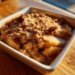 Close-up of a warm, bubbling single serving apple crisp recipe in a white square dish.