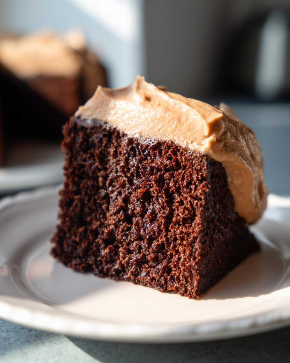 Close-up of a moist slice of dark gingerbread cake topped with light brown frosting.