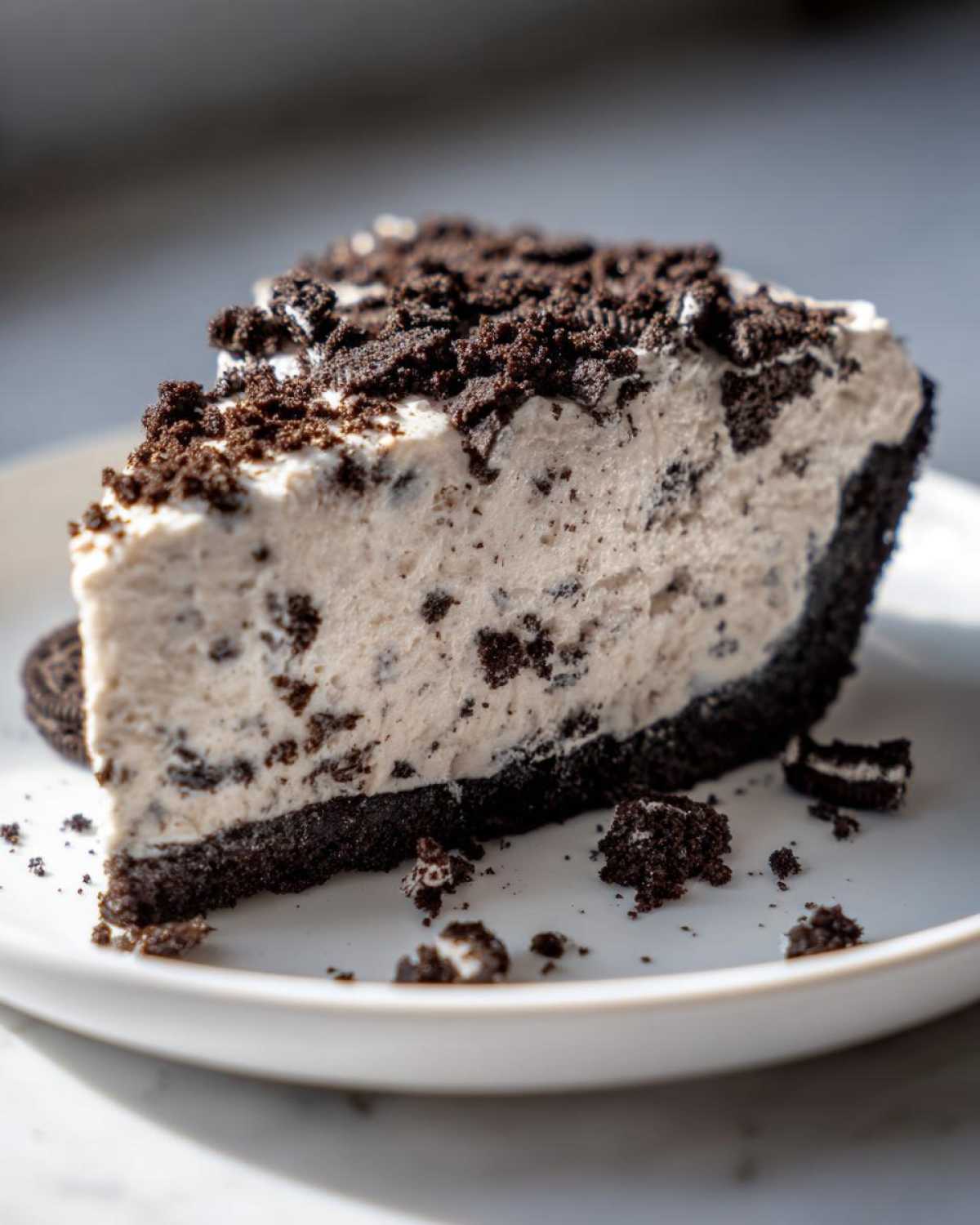 A generous slice of creamy Oreo pie with a dark chocolate crust, topped with cookie crumbs.