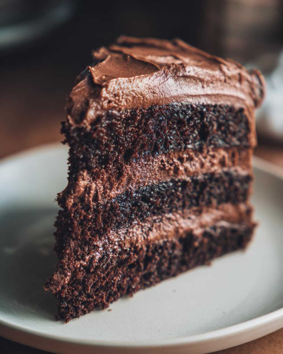 Close-up of a moist, triple-layer slice of chocolate cake recipe with thick chocolate frosting.