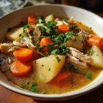 Close-up of a hearty bowl of slow cooker chicken stew featuring shredded chicken, large potato chunks, bright orange carrots, and fresh parsley.