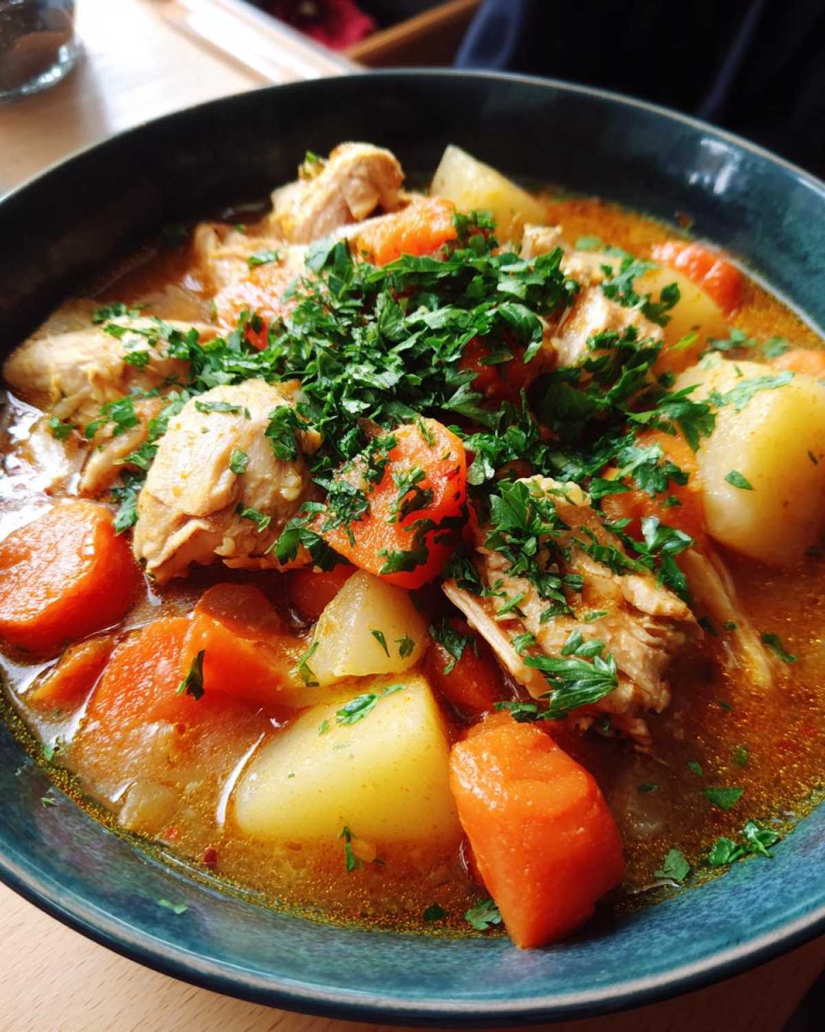 A close-up of a hearty bowl of slow cooker chicken stew featuring chunks of chicken, potatoes, carrots, and fresh parsley.