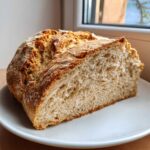 A thick slice cut from a homemade soda bread loaf showing its light, airy crumb and golden crust.
