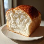 Close-up of a freshly baked japanese milk bread loaf showing its incredibly soft, fluffy white interior and golden-brown crust.