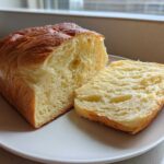 A freshly baked loaf of Japanese milk bread, partially sliced to show its incredibly soft, fluffy interior.