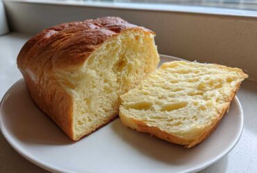 A freshly baked loaf of Japanese milk bread, partially sliced to show its incredibly soft, fluffy interior.