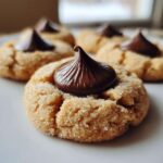 A close-up of a soft peanut butter kiss cookie rolled in sugar, topped with a melted chocolate kiss.