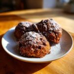 Three soft persimmon cookies dusted heavily with powdered sugar resting on a light gray plate.