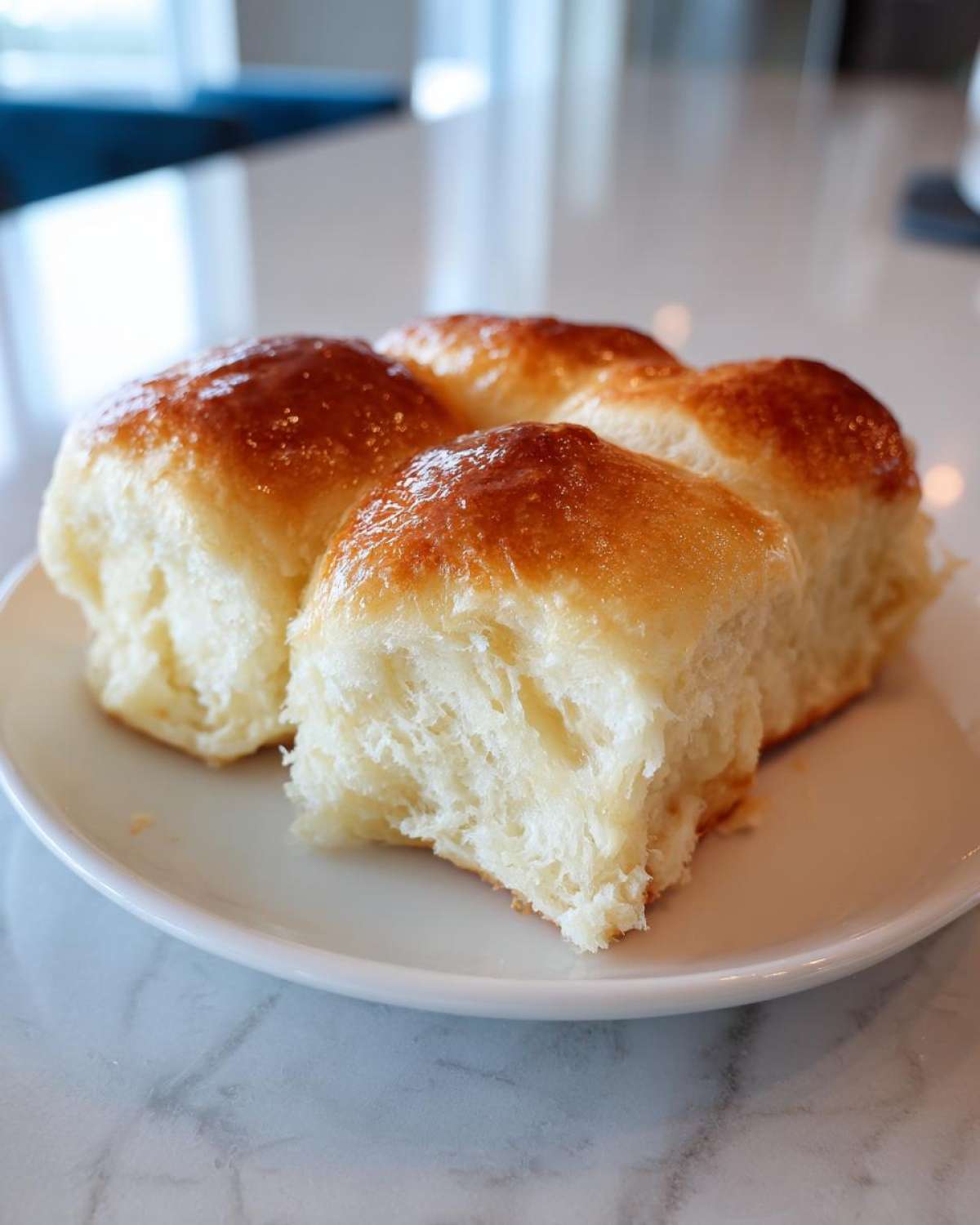 Four fluffy sourdough discard rolls with a shiny, golden-brown top, served on a white plate.