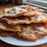 A tempting stack of freshly fried buñuelos generously coated in granulated sugar, resting on a white plate.