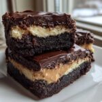 Two stacked squares of rich, three-layer buckeye brownies featuring a chocolate base, peanut butter filling, and chocolate ganache topping.
