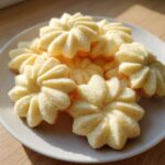 A pile of freshly baked, star-shaped butter cookie treats on a light plate, catching bright sunlight.