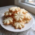 A pile of delicate, star-shaped whipped shortbread cookies with slightly browned edges on a white plate.