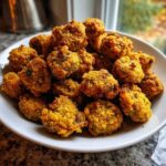 A close-up of a white bowl overflowing with golden brown, crispy fried okra pieces.
