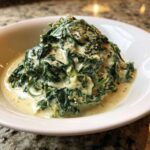 Close-up of a serving of rich creamed spinach recipe, topped with cracked black pepper, in a white bowl.