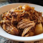Close-up of tender, shredded pork and sauerkraut mixture served in a white bowl.