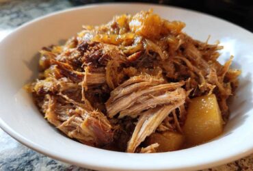 Close-up of tender, shredded pork and sauerkraut mixture served in a white bowl.